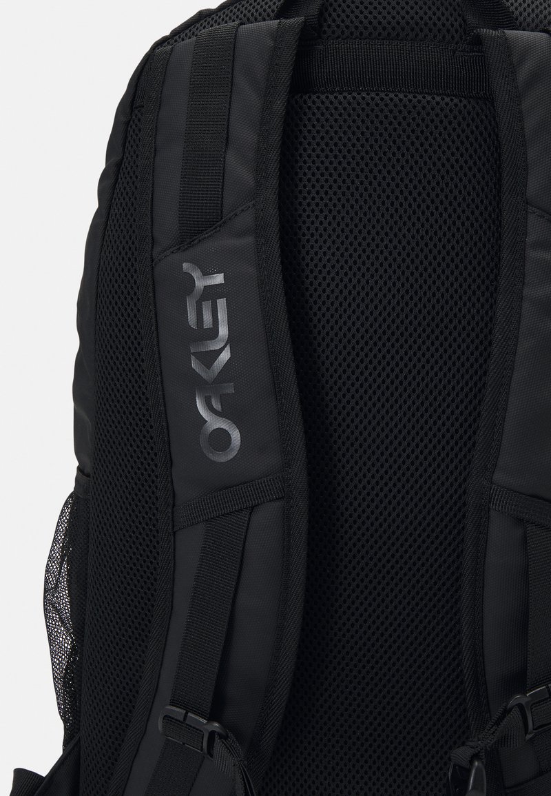 Black backpack featuring padded, mesh straps for comfort, durable material, and a silver logo on one strap. Textured back panel adds breathability.
