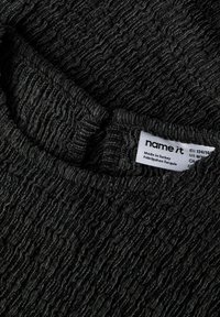 Pull sombre à texture ondulée, présentant un motif ondulé et un col rond. Étiquette d'entretien visible indiquant qu'il a été fabriqué en Turquie.