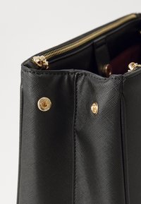 Schwarze synthetische Handtasche mit strukturierter Oberfläche, ausgestattet mit einem goldenen Reißverschluss und metallischen Akzenten. Das Innere zeigt ein bordeauxrotes Futter.