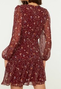 Blommönstrad klänning i vinröd genomskinlig tyg, med långa puffärmar, en figursydd midja och en flerlagrad volangkant.