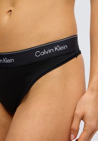 Must Calvin Kleini tanga laia elastse vöökohaga, millel on brändinimi valge kirjas. Siledat tekstuuri, keha järgiva lõikega.