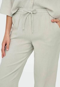 Pantalons gris clair texturés avec une taille élastique à cordon de serrage, des poches latérales et un design à coupe décontractée.