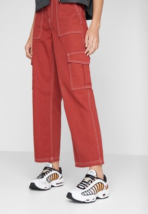 Persoon draagt rode wijde cargobroek met witte stiksels en witte Nike Max Air-sneakers met oranje en zwarte details.