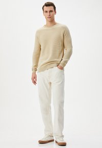 Beżowy sweter prążkowany, białe spodnie o prostym kroju i jasne sneakersy. Prosty design, miękka faktura i ciepłe neutralne kolory. Styl minimalistyczny.
