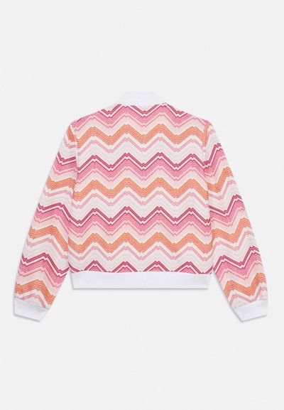 Veste à manches longues avec motif zigzag rose, rouge, orange et blanc, col blanc et poignets blancs, vue de dos sur un fond uni.