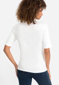 Witte top met korte mouwen, een soepele textuur, een ronde halslijn en een getailleerde snit, gecombineerd met donkerblauwe spijkerbroek.