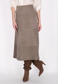 Grauer Wildleder-Midi-Rock mit einem Paneeldesign, das eine glatte Textur aufweist. Kombiniert mit braunen, lässigen Stiefeln bis zum Knie.