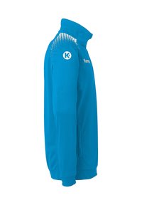 Lysblå zip-up jakke med høj krave, der har et tekstureret mønster på skuldrene og et logo på den øverste del af brystet.