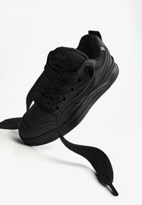 Pantof de sport negru cu un superior texturat, vârf rotund, talpă groasă și șireturi împletite negre. Dispune de orificii de ventilație și o bandă de prindere.