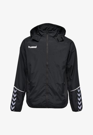 Chaqueta cortavientos negra con capucha, con cremallera frontal, bolsillos laterales y detalles en chevron blanco a lo largo de las mangas. Logotipo de Hummel visible.