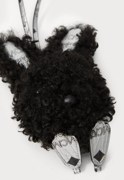 Accesoriu din pluș negru în formă de iepure, cu textură ondulată, având urechi gri cu logo-uri imprimate, ochi rotunzi și cleme din metal argintiu.