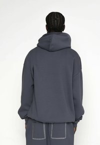 Szary, oversize'owy hoodie z dużym kapturem, ściągaczami przy rękawach i elastycznym dołem, z dekoracyjnymi przeszyciami na plecach i w okolicy kieszeni.