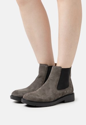 Grå suede ankelstøvler med elastiske sidestykker, rund tå og sort gummisål. Glat tekstur med et minimalistisk design.