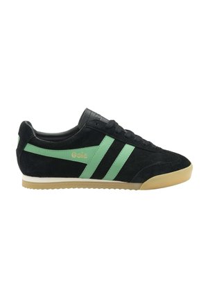 Zapatilla deportiva de ante negro con rayas verdes, suela beige, cordones en la parte delantera y logo "Gola" en el lateral, vista desde el lado exterior.