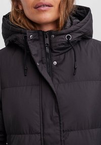 Veste rembourrée matelassée noire avec un col haut, une capuche ajustable, un zip frontal et des fermetures à bouton-pression. Tissu lisse et résistant à l'eau.