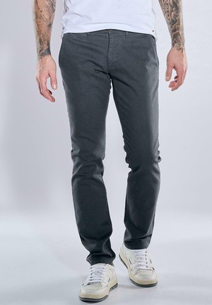 Grau Baumwollhosen mit slim Fit und subtiler Textur. Sie verfügen über einen Standardbund und einen Reißverschluss, kombiniert mit weißen Sneakers.