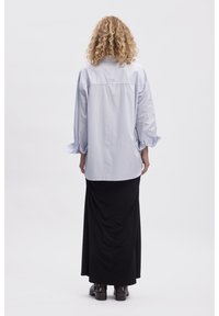 Light blue oversized shirt with long sleeves, button cuffs, back pleat detail. Paired with a black, ankle-length skirt and ankle boots.