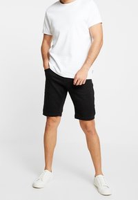Black denim shorts with a regular fit, a simple design, five pockets, and belt loops, paired with a plain white t-shirt and white sneakers.