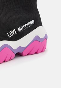 Black sneaker with a textured fabric upper. Features a white “LOVE MOSCHINO” logo and a multicolored sole in white, purple, and pink.