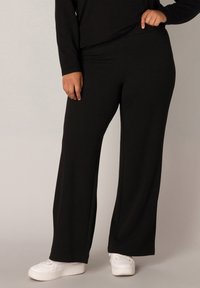 Zwarte wijde broek van zacht materiaal met een elastische tailleband. Gecombineerd met witte sneakers. Eenvoudig, casual ontwerp zonder patronen.