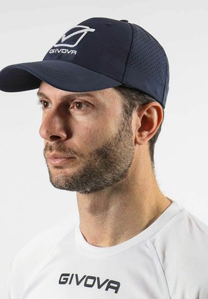 Uomo con barba corta che indossa un berretto GIVOVA blu navy e una maglia sportiva bianca GIVOVA, rivolto verso sinistra su uno sfondo chiaro e semplice.