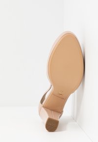 Chaussure à talon nude avec un bout arrondi, en matériau synthétique lisse, et une semelle en caoutchouc texturé dotée d'un petit talon et du logo de la marque.