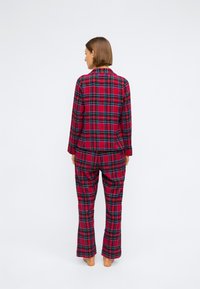 Rød rutete flanell pysjamas-sett med lange ermer og løse bukser, med et sjakkmønster med grønne og sorte detaljer.