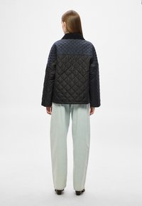 Μπουφάν μαύρο καπιτονέ με κομψό cropped σχέδιο, διαθέτει γιακά, μακριά μανίκια και αντιθετικά πάνελ. Συνδυασμένο με ανοιχτό μπλε τζιν παντελόνι φαρδιάς γραμμής.