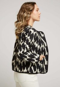 Veste matelassée avec un motif ikat noir et blanc, un col rond et des poches latérales. Le tissu présente une apparence texturée et gonflée.