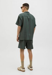 T-shirt à manches courtes, de couleur vert foncé, côtelé, avec un short assorti ; en tissu léger, coupe décontractée et ourlets roulés ; associé à des baskets beiges.