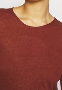 Röd t-shirt med kort ärm, tillverkad av lättviktig, strukturerad tyg med rund halsringning, som har ett subtilt melerat mönster.