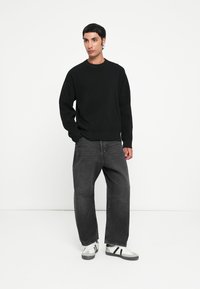 Svart ribbestrikket genser med lange ermer, sammen med løse, mørkegrå jeans og hvite sneakers med svarte striper.