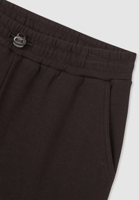 Ciemnobrązowe spodnie dresowe z teksturowanej tkaniny, elastycznym pasem w talii z zapięciem na przewleczoną linkę oraz boczną kieszenią.