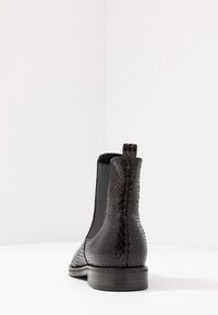 Černá kožená chelsea boot s texturovaným vzorem hadí kůže, elastickými bočními panely a nízkým dřevěným podpatkem. Zadní pohled ukazuje detail s poutkem.