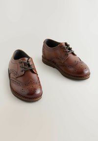 Chaussures en cuir marron avec des détails en brogue, bout rond et fermeture à lacets. Caractéristiques intérieures noires et bords cousus pour une durabilité accrue.