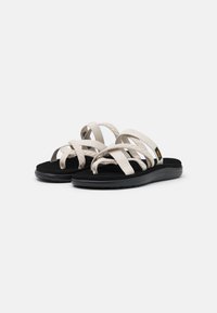 Lichtbeige sandalen met gekruiste banden, zwarte zool en een gestructureerde voetbed. Ontworpen voor comfort, met flexibele en duurzame materialen.