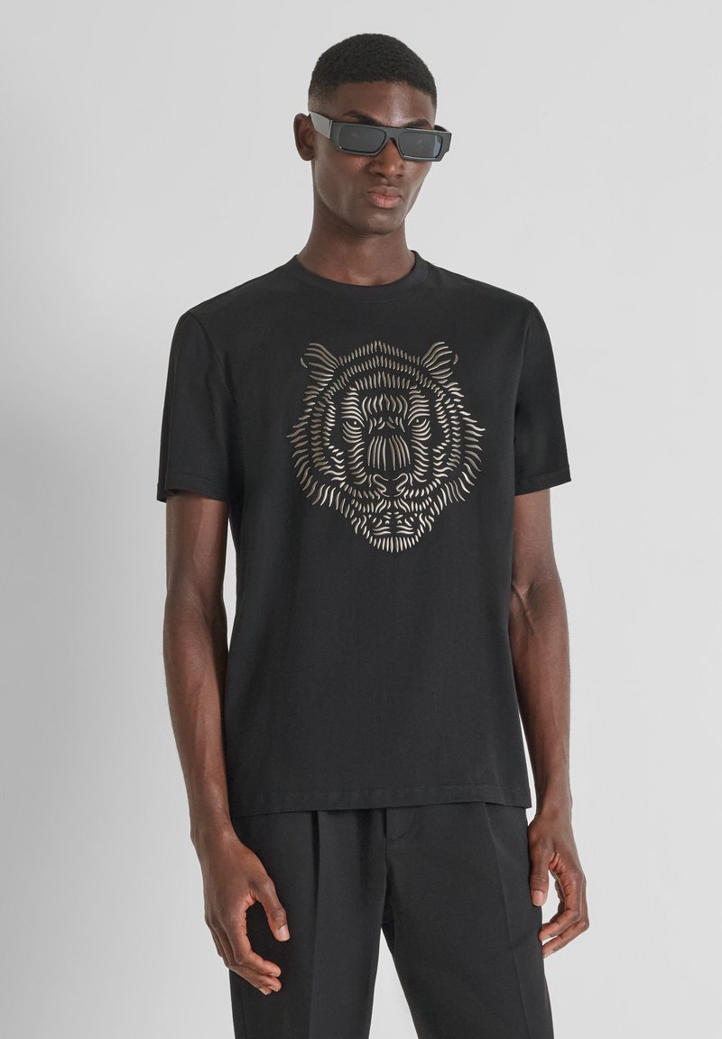 Camiseta de algodón negra con un detallado gráfico de tigre en dorado metálico. Manga corta, cuello redondo, corte relajado y textura suave.