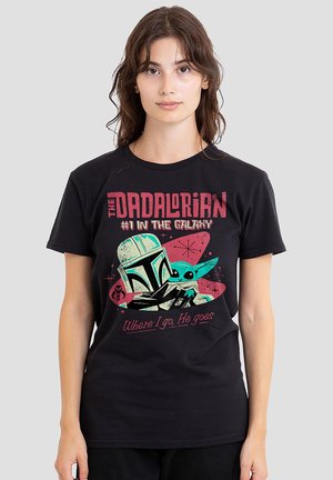 Frau trägt ein schwarzes T-Shirt mit Grafik eines Mandalorian-Helms und Baby Yoda, Text: "The Dadalorian #1 in der Galaxie" und "Wo ich hingehe, geht er hin."