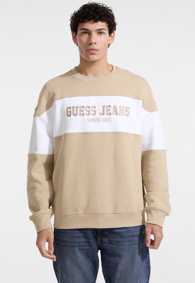 Beżowa i biała bluza z okrągłym dekoltem, ściągaczami oraz subtelnym nadrukiem "GUESS JEANS SINCE 1981" z przodu.