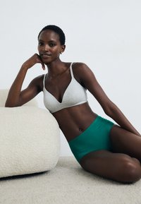 Harmaa kolmiomallinen bralette, jossa on ohuet hihnat, yhdistetty vihreisiin korkeavyötäröisiin alushousuihin. Molemmissa vaatteissa on pehmeä rakenne, ja ne on asetettu vaaleaa taustaa vasten.