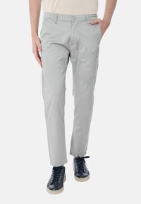 Pantaloni in cotone grigio chiaro con taglio dritto, dotati di chiusura con bottone, tasche laterali, indossati con sneakers nere.
