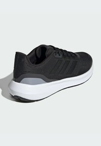 Zapatilla deportiva negra con parte superior texturizada, que presenta tres rayas negras en el lateral, una suela blanca acolchada y acentos grises cerca del talón.