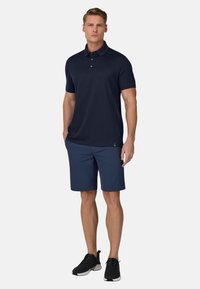 Polo da uomo blu navy con maniche corte, abbinata a pantaloncini blu navy scuro e scarpe da ginnastica nere. Presenta una patta con tre bottoni.