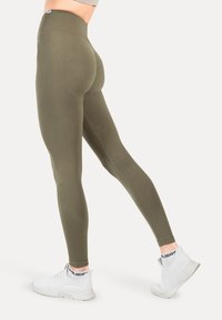 Olivgröna tights med hög midja och texturerad yta. Kombineras med vita träningsskor med en svart och vit logotyp på remmen.