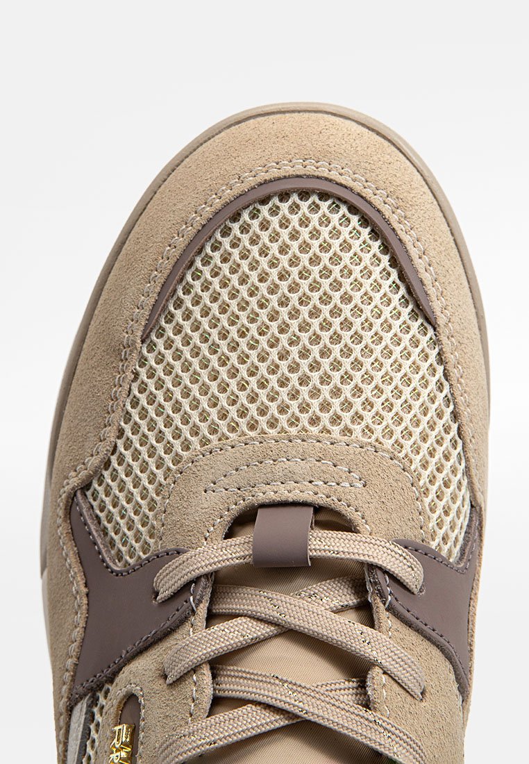 Chaussure de sport beige avec une tige en daim et des panneaux en mesh. Dotée de accents marron et de lacets plats. Vue en gros plan de la zone des orteils et du laçage.