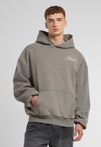Gray oversized hoodie with a front pocket, ribbed hem, and cuffed sleeves. Features subtle branding in light embroidery. Soft fabric texture.