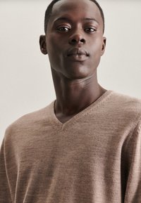 Brauner Woll-V-Ausschnitt-Pullover mit texturiertem Finish und subtilen Nähten. Die Passform ist locker und sorgt für eine bequeme Silhouette.