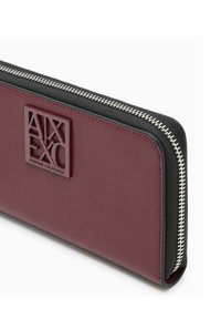 Portafoglio bordeaux e nero con cerniera argentata, dotato di logo Armani Exchange in rilievo sul pannello frontale.