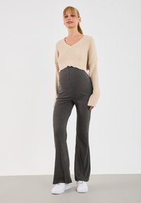 Pull court en tricot côtelé beige clair avec un col en V, associé à un pantalon évasé côtelé gris et des baskets blanches. Tenue simple et décontractée.