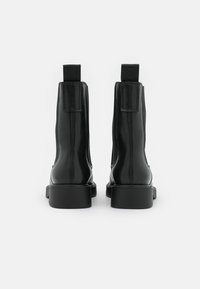Černé kožené kotníkové boty s elastickými bočními paneli, plochou podrážkou a poutky vzadu, s hladkou texturou a minimalistickým designem.